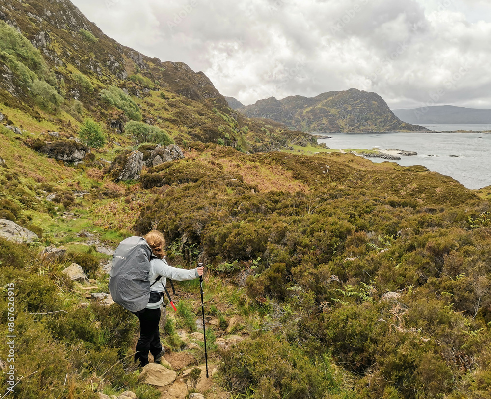 Naklejka premium Woman with hiking poles and hiking backpack looking at coastal landscape in west coast of Scotland