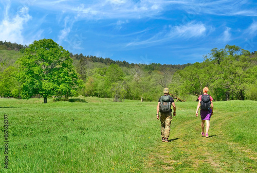 Back view photo of couple tourists backpacker walking on trail and viewing a beautiful landscape in spring sunny day.  © Jurek Adamski