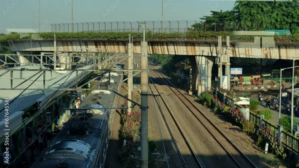 Station scenery with yellowish morning sunlight, trains leaving, passengers waiting by the tracks, long power lines, tracks, traffic and surrounding suburbs. Station scenery with yellowish morning sunlight, trains leaving, passengers waiting by the tracks, long power lines, tracks, traffic and surrounding suburbs.