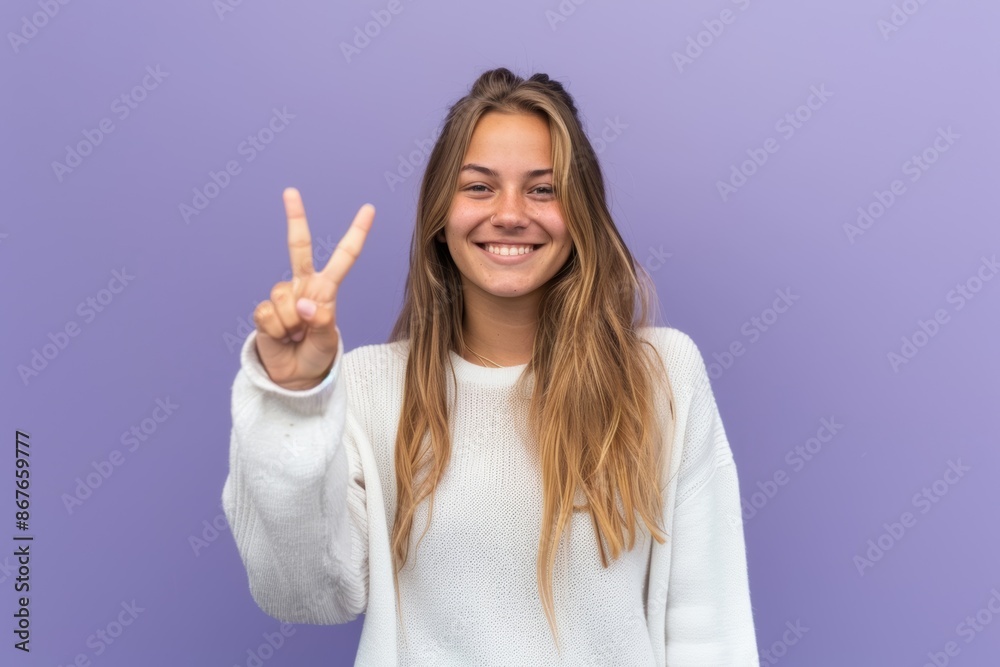 Smiling Woman in White Sweater Giving Peace Signs Against Purple Background Smiling Woman in White Sweater Giving Peace Signs Against Purple Background