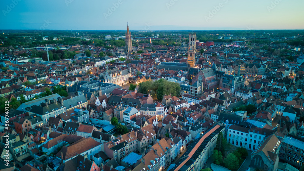 Obraz premium Enchanting aerial view of Bruges' historic old town captured by a drone at night! The illuminated medieval architecture, winding canals, and charming cobblestone streets create a magical and captivati