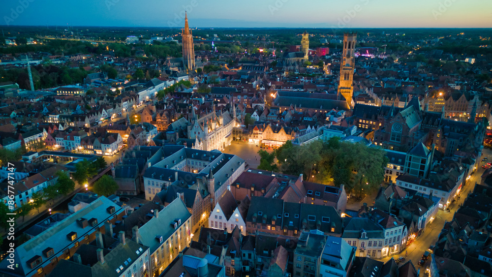 Obraz premium Enchanting aerial view of Bruges' historic old town captured by a drone at night! The illuminated medieval architecture, winding canals, and charming cobblestone streets create a magical and captivati