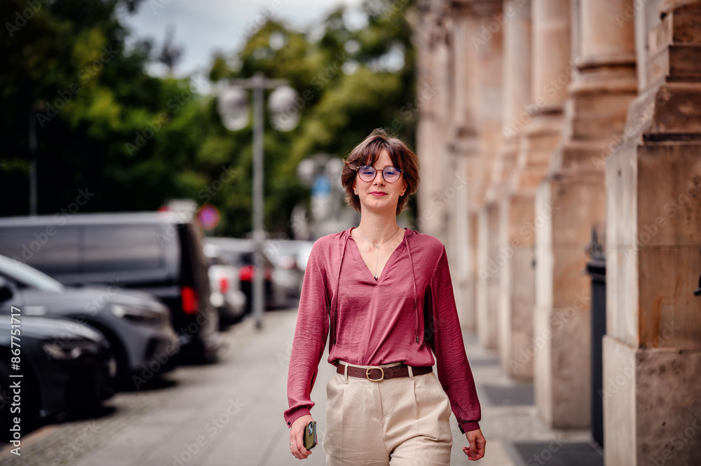 Woman in casual attire smiling while walking on a city sidewalk lined with parked cars and buildings. Woman in casual attire smiling while walking on a city sidewalk lined with parked cars and buildings.