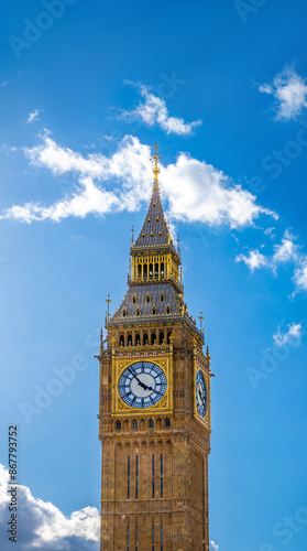 Obraz na płótnie Top view of the Big Ben Clock Tower seen in full detail of its gold ornamentation and cross capital on a bright day with clear blue sky and backlit clouds