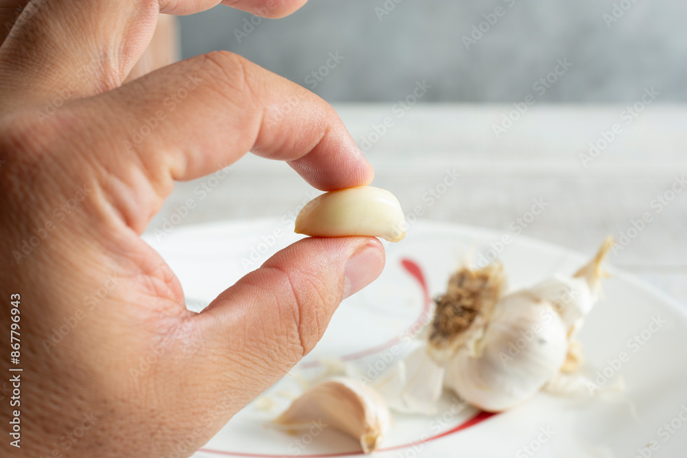 A view of a hand holding a peeled garlic clove. A view of a hand holding a peeled garlic clove.
