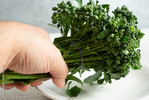 A view of a hand holding a bundle of broccolini over a plate. photo