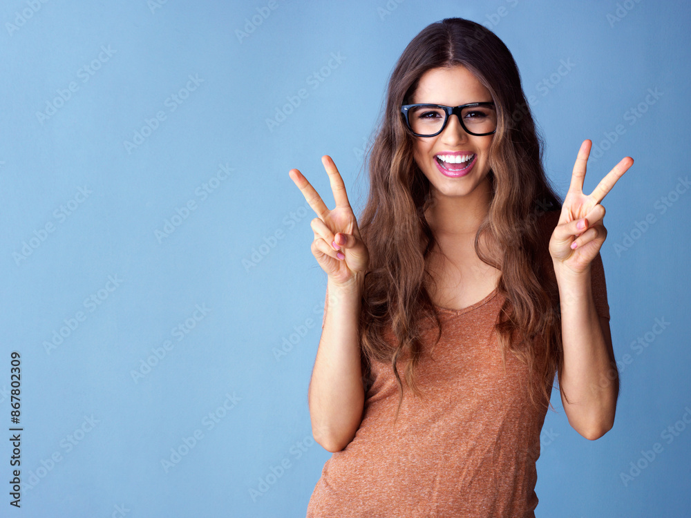 Portrait, hands and happy woman with peace sign in studio for excitement, good mood or expression on blue background. V, emoji and model with glasses for gesture, positive attitude or smile mockup Portrait, hands and happy woman with peace sign in studio for excitement, good mood or expression on blue background. V, emoji and model with glasses for gesture, positive attitude or smile mockup