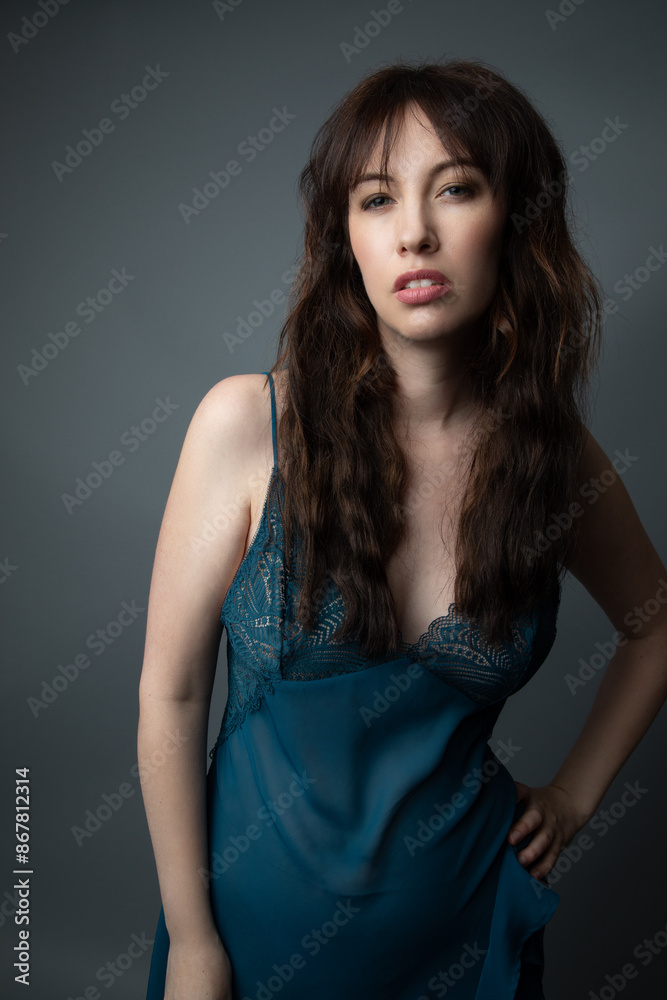 Fototapeta premium Studio portrait of a beautiful caucasian woman in her 30s wearing a dark blue nightgown. She has brown hair and blue eyes. The background is grey. 