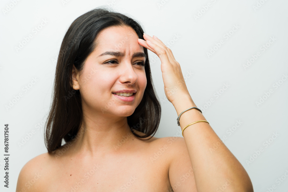 Graceful latina woman delicately touches her forehead and expression lines in a simple studio backdrop Graceful latina woman delicately touches her forehead and expression lines in a simple studio backdrop