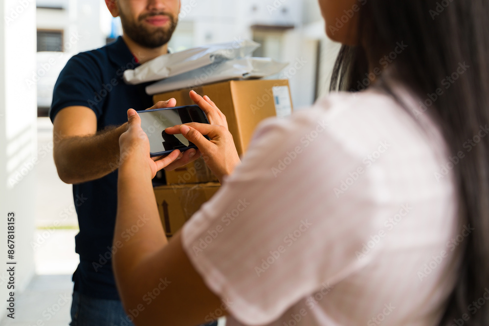 Delivery man hands cardboard boxes to a young woman as she signs on a smartphone to receive a package Delivery man hands cardboard boxes to a young woman as she signs on a smartphone to receive a package