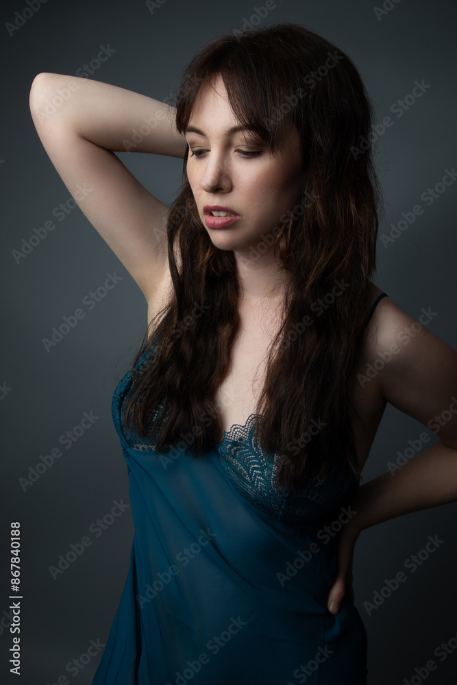 Studio portrait of a beautiful caucasian woman in her 30s. She is wearing a royal blue nightgown. She is looking downwards. She has long wavy brown hair and full lips. Studio portrait of a beautiful caucasian woman in her 30s. She is wearing a royal blue nightgown. She is looking downwards. She has long wavy brown hair and full lips.