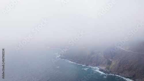 A drone captures the foggy aerial view of Californias Big Sur coast along Highway 1, displaying the areas natural beauty in a rugged landscape with stunning cliffs and the vast ocean