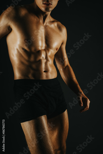 Fit man showing his abs, highlighting his muscular body and fitness. Taken in a dark background to emphasize the physique. © qunica.com