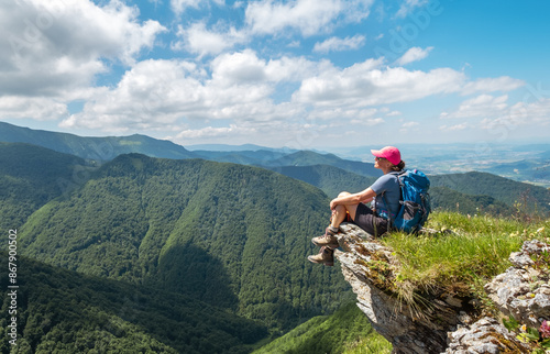 Dressed trekking clothes hiker woman sitting on rocky cliff enjoying green valley at Mala Fatra mountain range, Slovakia. Active people and European tourism concept image.