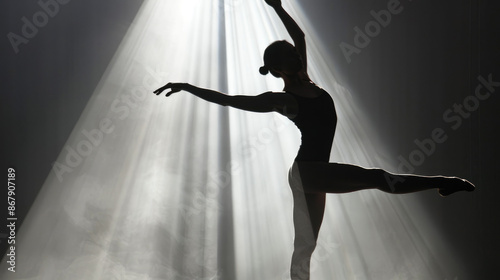 A ballet dancer performs an elegant arabesque pose on stage, bathed in dramatic beams of light, creating a sense of grace and focus.