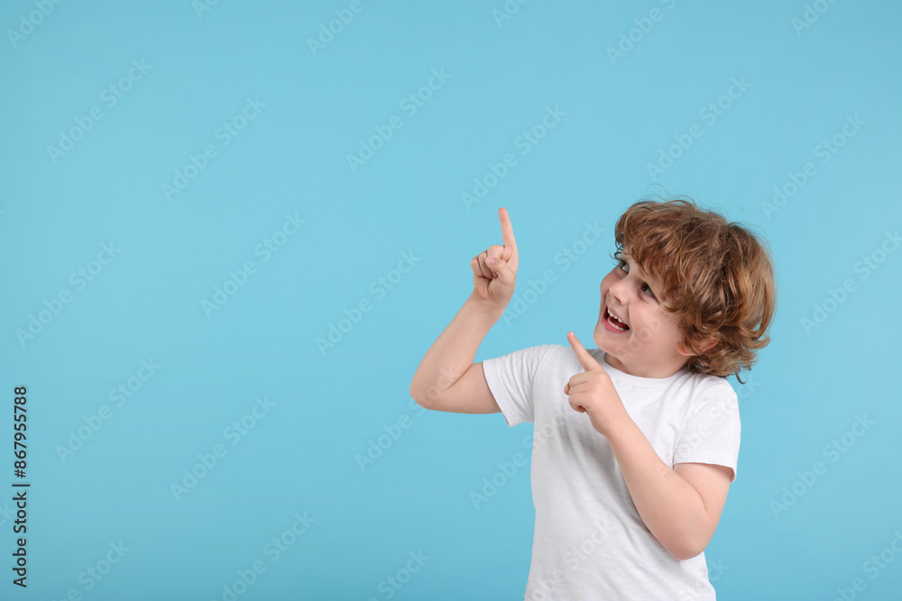 Cute little boy pointing at something on light blue background, space for text Cute little boy pointing at something on light blue background, space for text