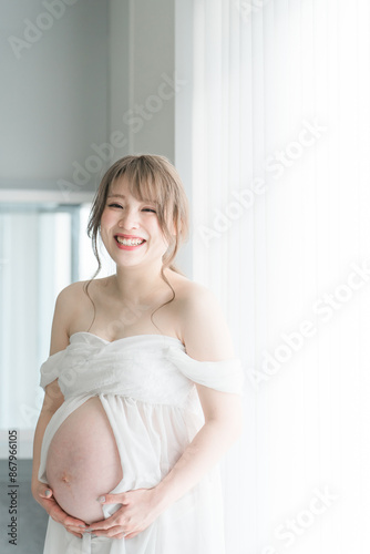 Free Download 家のカーテンの前でマタニティフォトの撮影をする妊婦のアジア人女性
 - GFXLoad