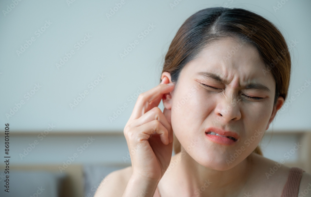Asian woman having an earache problem. An earache is sharp, dull, or burning ear pain in one or both ears.