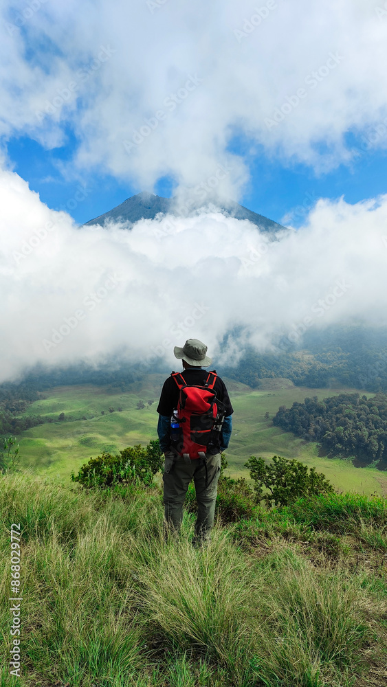 Young man is looking at the peak of Mount Rinjani from the kondo hills of Lombok, Indonesia. the landscape is for hiking and outdoor lifestyle concept. beautiful natural scenery Young man is looking at the peak of Mount Rinjani from the kondo hills of Lombok, Indonesia. the landscape is for hiking and outdoor lifestyle concept. beautiful natural scenery
