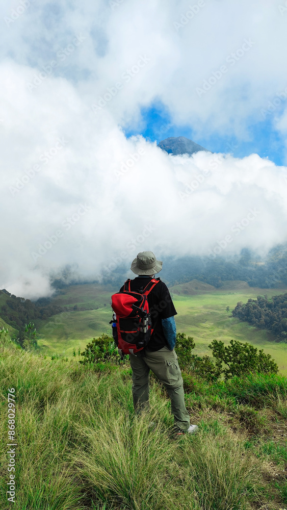 Young man is looking at the peak of Mount Rinjani from the kondo hills of Lombok, Indonesia. the landscape is for hiking and outdoor lifestyle concept. beautiful natural scenery Young man is looking at the peak of Mount Rinjani from the kondo hills of Lombok, Indonesia. the landscape is for hiking and outdoor lifestyle concept. beautiful natural scenery