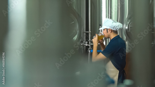 A young Asian worker checks the quality of a brewery by tasting a glass of craft beer. photo