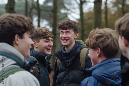 Close waist-up in Rothbury's woodlands, a group of male student teenagers are on an educational walk. They explore nature, blending lessons with the outdoors. They are standing in a circle, smiling an photo