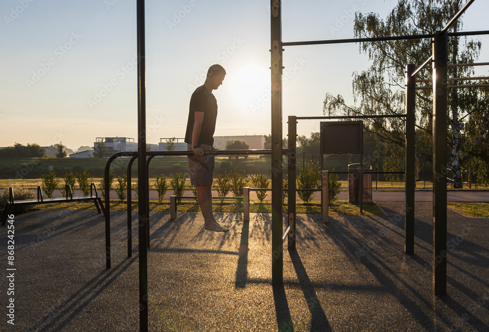 Fototapeta premium Fitness man doing dips on the work out playground at sunrise. Morning routine, mental and physical strength, healthy lifestyle background