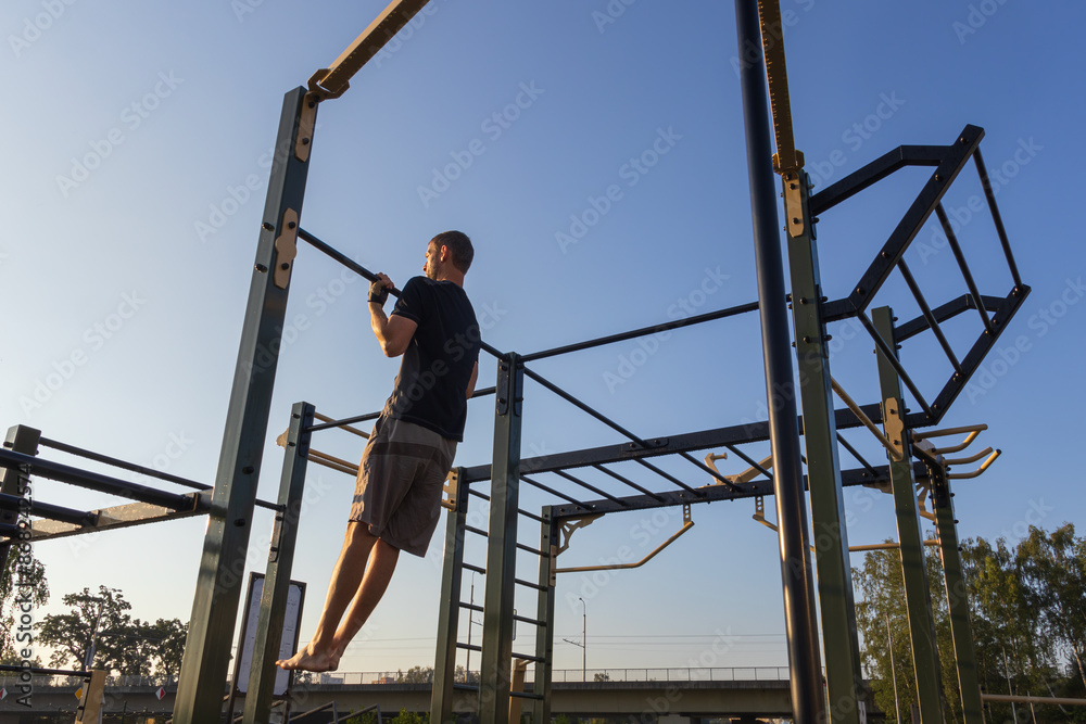 Fitness man doing pull ups on the work out playground at sunrise. Morning routine, mental and physical strength, healthy lifestyle background Fitness man doing pull ups on the work out playground at sunrise. Morning routine, mental and physical strength, healthy lifestyle background
