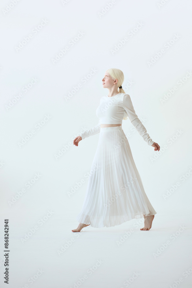 Pretty albino teen girl, beautiful barefoot unique model in white walking on tip toes in white studio background. Inclusive unusual natural beauty, inclusion, albinism, vertical full body photo. Pretty albino teen girl, beautiful barefoot unique model in white walking on tip toes in white studio background. Inclusive unusual natural beauty, inclusion, albinism, vertical full body photo.