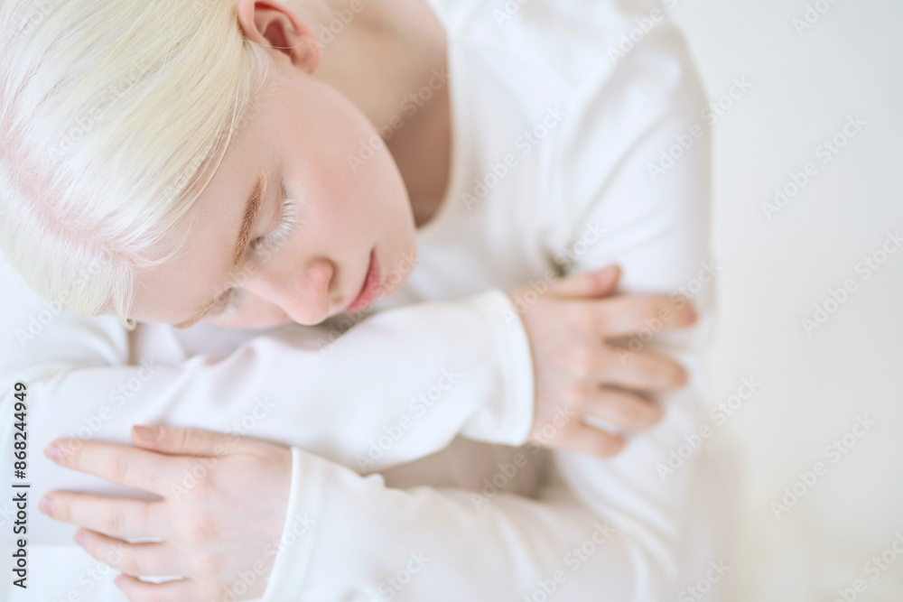Vulnerable albino teen girl, beautiful unique woman model in white sitting on white studio background. Inclusive unusual natural beauty face, inclusion, albinism and diversity, close up portrait. Vulnerable albino teen girl, beautiful unique woman model in white sitting on white studio background. Inclusive unusual natural beauty face, inclusion, albinism and diversity, close up portrait.