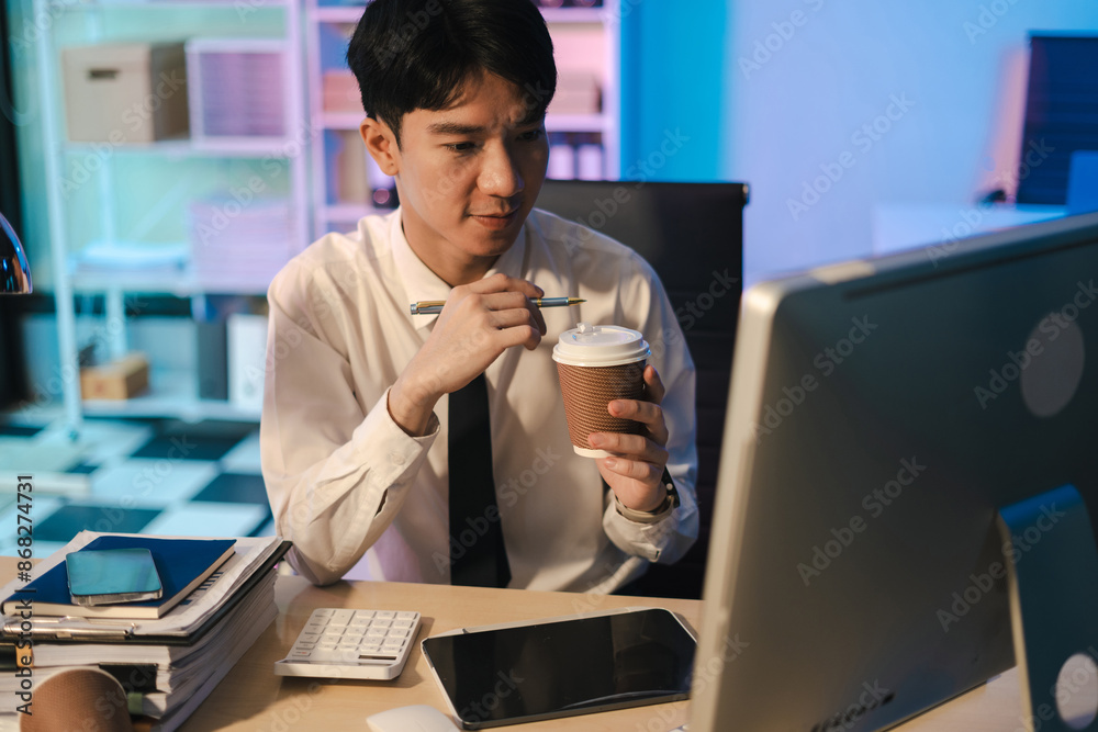 Tired, office worker sitting at a desk using a computer and doing projects overtime in the office.