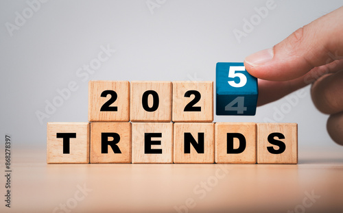 Foto Hand flipping wooden block cube to change from 2024 to 2025 trends for business , fashion and technology trend change concept after new year
