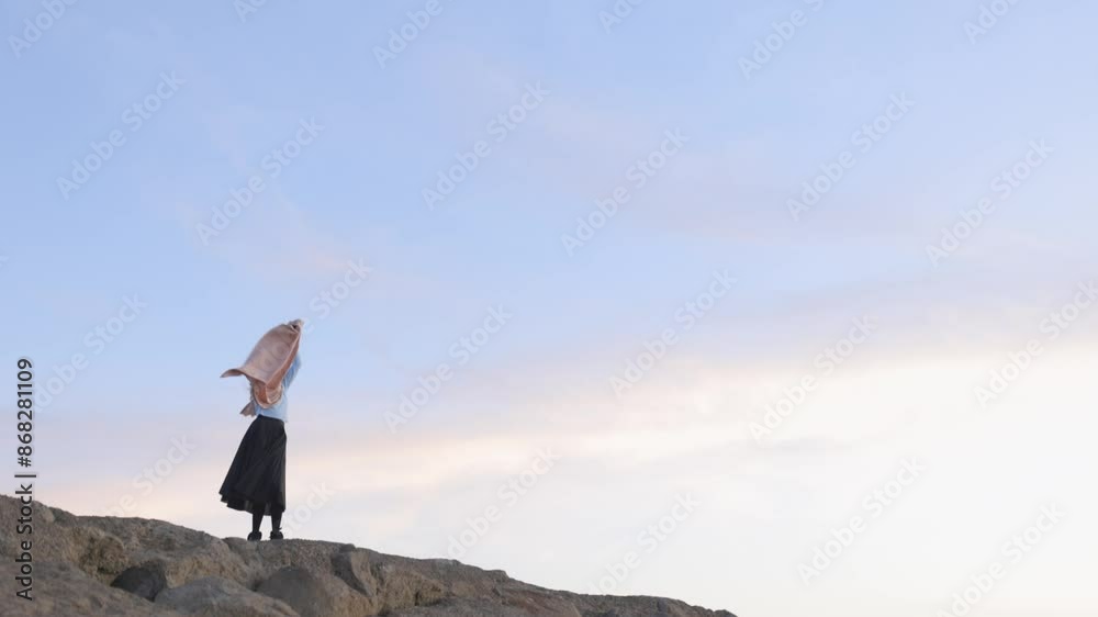 A woman is standing on a rocky hillside, wearing a blue shirt and black skirt A woman is standing on a rocky hillside, wearing a blue shirt and black skirt