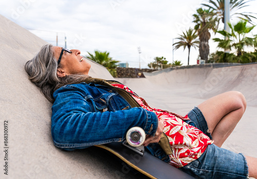 Beautiful confident senior woman with grey hair skateboarding outdoors