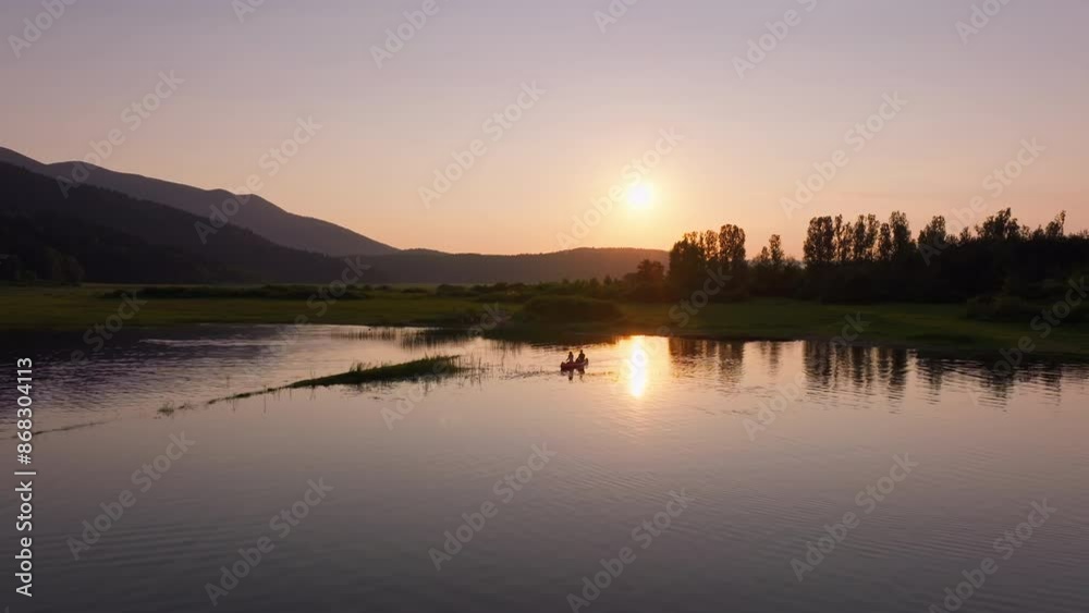 Couple canoeing at sunset, two silhouettes paddling a canoe on a beautiful lake in the evening, aerial shot. Nature enjoyment and relaxation concepts. Couple canoeing at sunset, two silhouettes paddling a canoe on a beautiful lake in the evening, aerial shot. Nature enjoyment and relaxation concepts.