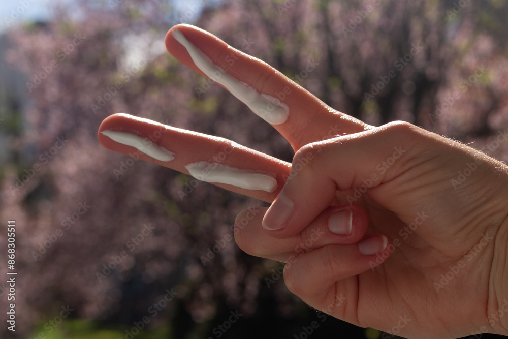 A person applying the correct amount of sunscreen for the face and neck – two finger lengths, with cherry blossom trees in the background. Concept of applying sunscreen in spring.