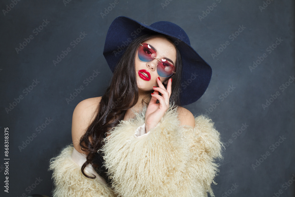 Posing fashion model woman with long dark wavy hairstyle and red lips make-up wearing fashionable hat beauty studio portrait Posing fashion model woman with long dark wavy hairstyle and red lips make-up wearing fashionable hat beauty studio portrait
