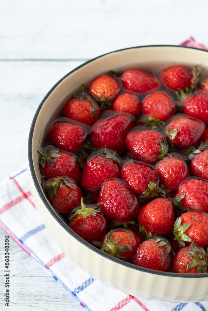 Strawberries in a bowl with fresh water on wooden table. Close-up. Washing and cleaning organic sweet berries before eating. Strawberries in a bowl with fresh water on wooden table. Close-up. Washing and cleaning organic sweet berries before eating.