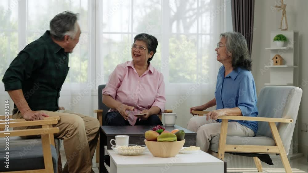 Handheld video of Senior Asian friends enjoying retirement together. Woman holding playing cards, engaged in conversation with man and woman. Bright living room setting Casual, relaxed atmosphere. Handheld video of Senior Asian friends enjoying retirement together. Woman holding playing cards, engaged in conversation with man and woman. Bright living room setting Casual, relaxed atmosphere.