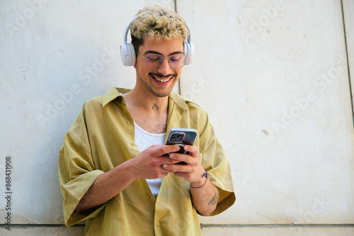 Obraz na płótnie A man with a beard and glasses is smiling while holding a cell phone. He is wearing headphones and he is listening to music w salonie
