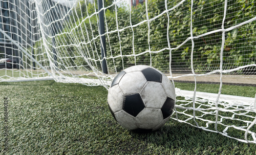 Soccer football in Goal net with green grass field.