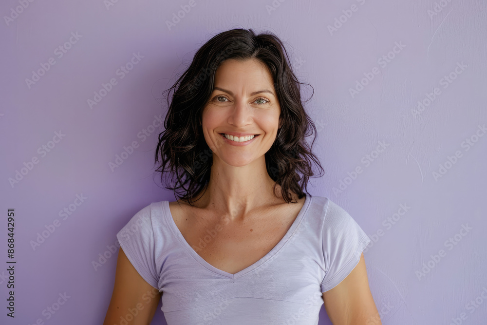 Fototapeta premium A woman with curly hair and a genuine smile wears a v-neck t-shirt against a soothing purple background