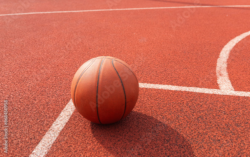 Above view sports background of orange basketball ball lying on court floor lit by sunlight, copy space