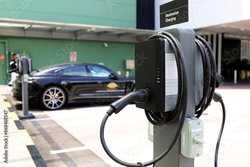 Fototapeta Naklejka Na Ścianę i Meble -  EV electric car charger box in parking lot. Urban sustainability lifestyle with environmentally friendly and clean rechargeable energy from the inside of electric BEV vehicles.