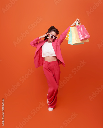 Happy pretty shopaholic woman carrying colorful shopping bags isolated on orange studio background..
