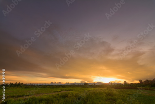 Golden Evening Light: Peaceful Meadow, Mountains, and Orange Sky - Ideal for Background Design © suwatsilp