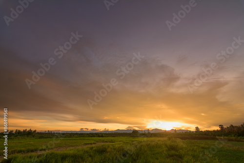 Fototapeta Naklejka Na Ścianę i Meble -  Golden Evening Light: Peaceful Meadow, Mountains, and Orange Sky - Ideal for Background Design