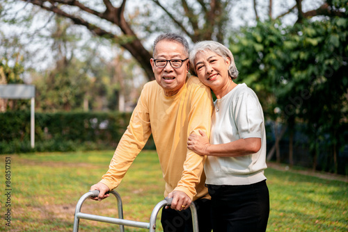 A couple of older people are standing in a grassy area, one of them holding a walker