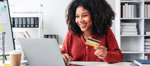 A woman is smiling while holding a credit card in front of a laptop