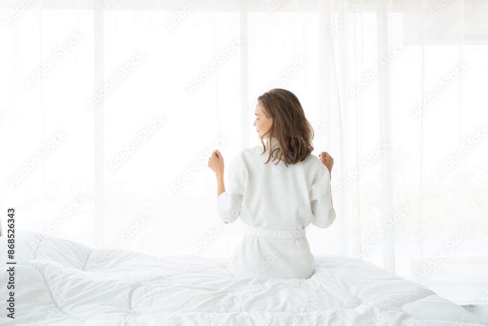 Woman stretching in bed after wake up. she sitting near the big white window while stretching on bed after waking up with sunrise at morning Woman stretching in bed after wake up. she sitting near the big white window while stretching on bed after waking up with sunrise at morning